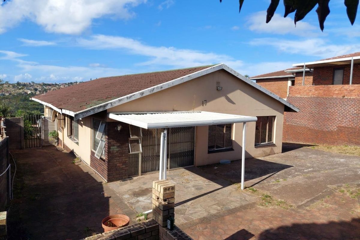 Rear view of the property featuring a covered patio area, paved yard, and brick boundary walling.