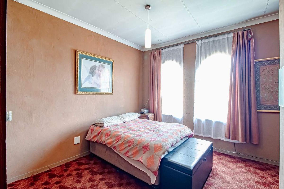A bedroom featuring dual windows with curtains, carpeted flooring, and a central pendant light fixture.
