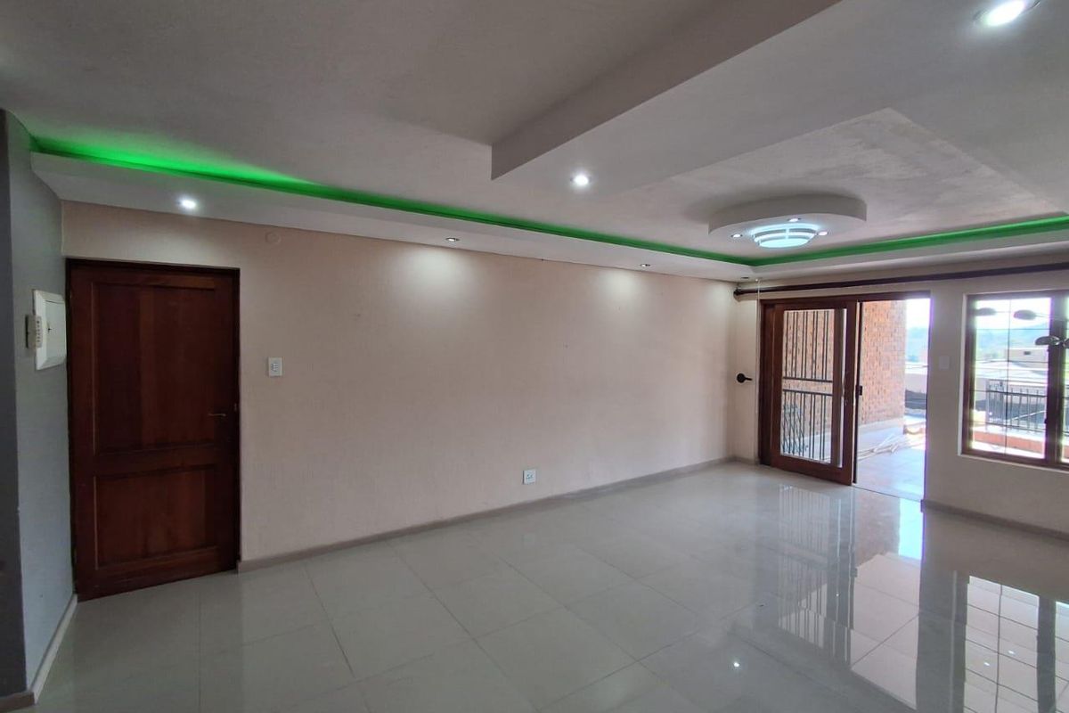Spacious, empty living area featuring polished tiled floors, recessed ceiling lighting with green LED accents, and direct access to an outdoor balcony.
