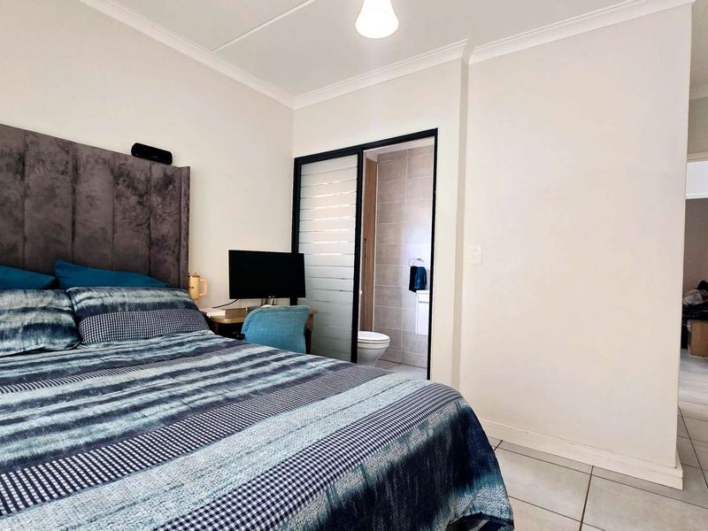 A well-maintained bedroom featuring tiled flooring, coved ceilings, and direct access to an en-suite bathroom through a sliding door.