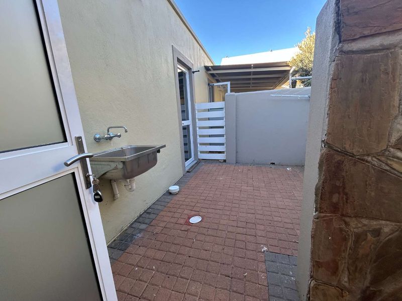 A functional outdoor laundry courtyard featuring a stainless steel utility sink, paved flooring, and a wall-mounted drying rack.
