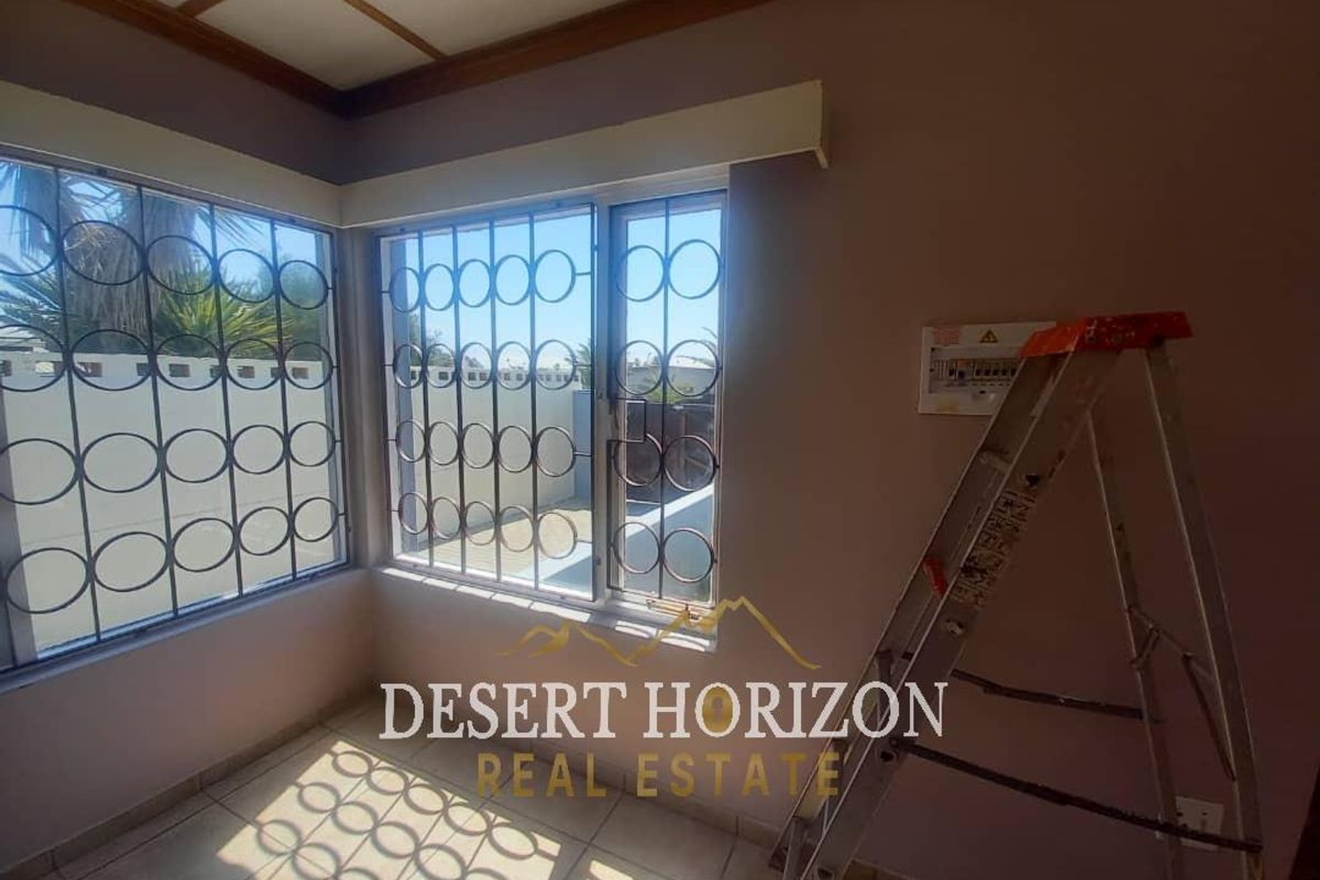A sunlit room featuring large windows with decorative security bars, tiled flooring, and a coffered ceiling detail.