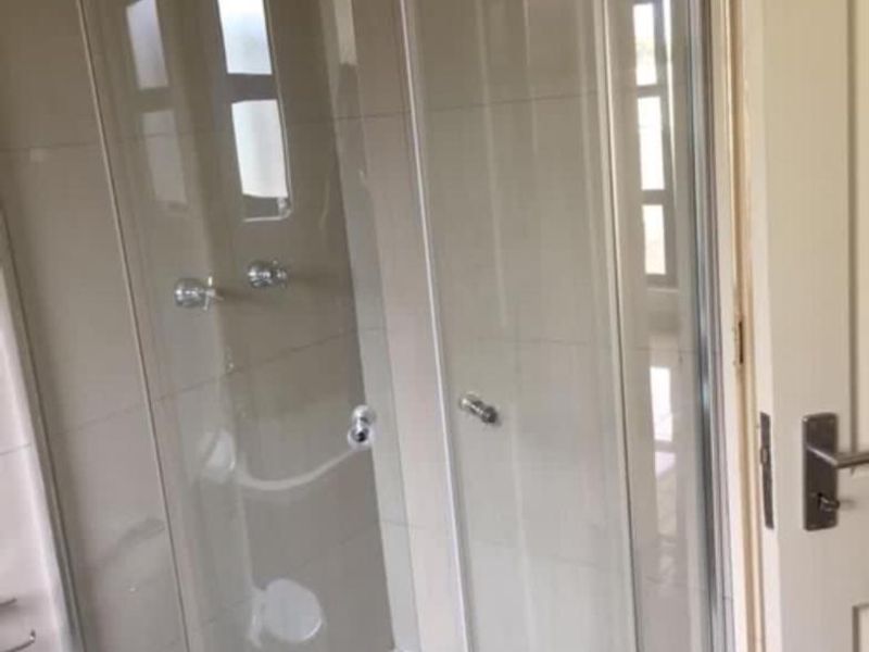 A functional bathroom featuring a corner shower enclosure with tiled walls and chrome fixtures.
