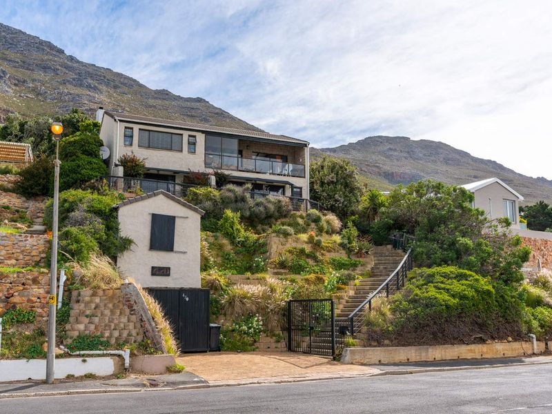 Elevated multi-level residential property featuring stone retaining walls, a private staircase, and a balcony with mountain views.