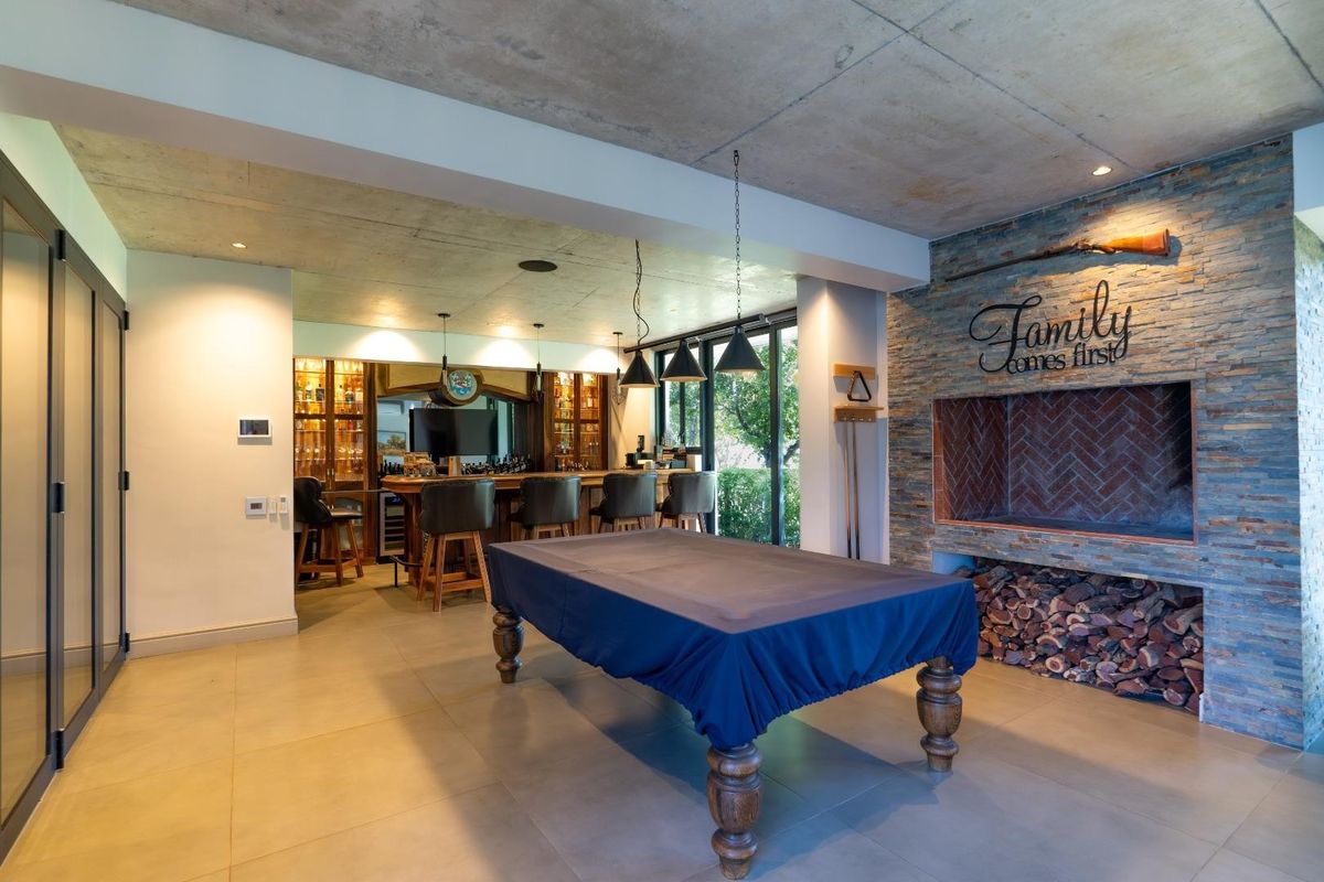 Spacious entertainment area featuring an exposed concrete ceiling, stone-clad fireplace with integrated wood storage, and a custom built-in bar.