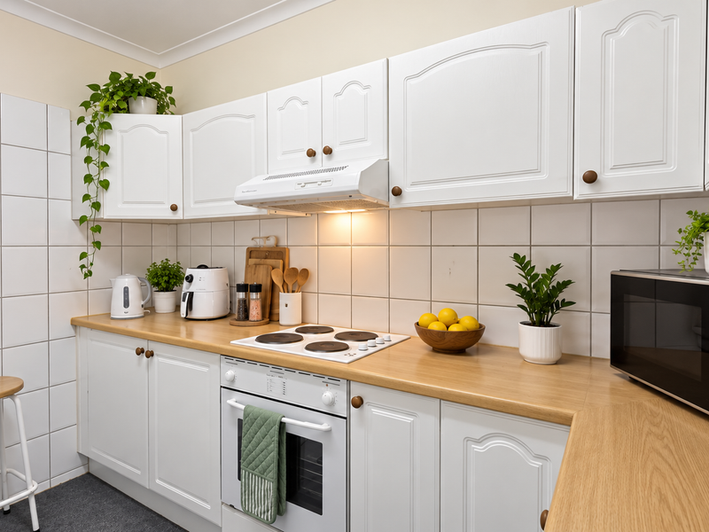 A functional kitchen featuring white cabinetry, light wood-tone laminate countertops, a tiled backsplash, and integrated cooking appliances.
