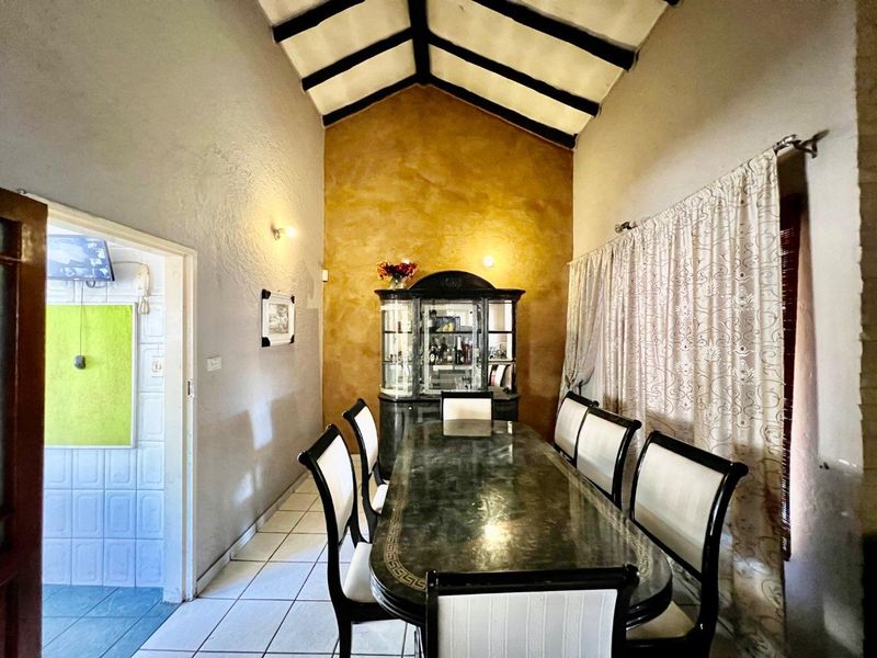 A dining room featuring a high vaulted ceiling with exposed timber beams, tiled flooring, and a textured feature wall.