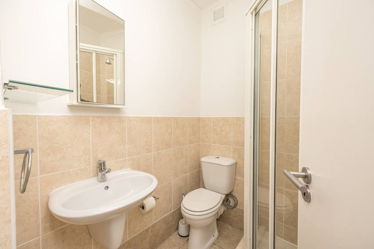 A compact bathroom featuring a pedestal sink, a toilet, and a glass-enclosed shower stall with neutral wall tiling.
