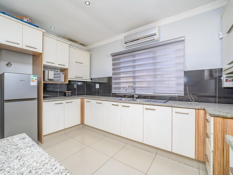A functional kitchen featuring white and wood-tone cabinetry, granite countertops, tiled flooring, and a wall-mounted air conditioning unit.