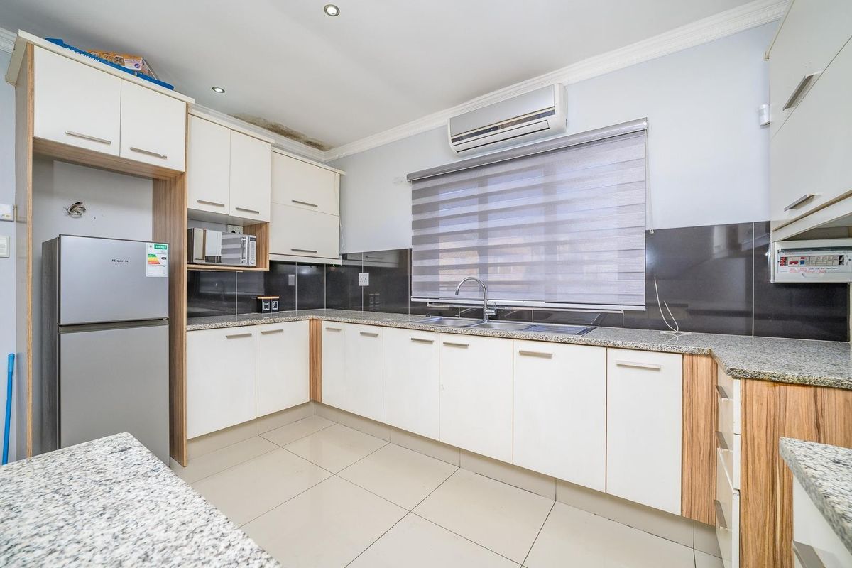 A functional kitchen featuring white and wood-tone cabinetry, granite countertops, tiled flooring, and a wall-mounted air conditioning unit.