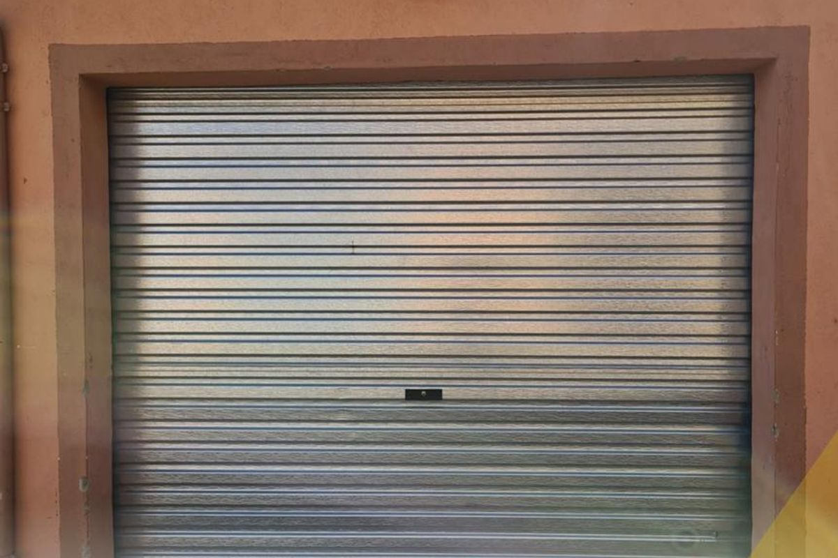 A secure garage featuring a metal roller shutter door and an exterior wall-mounted light fixture.