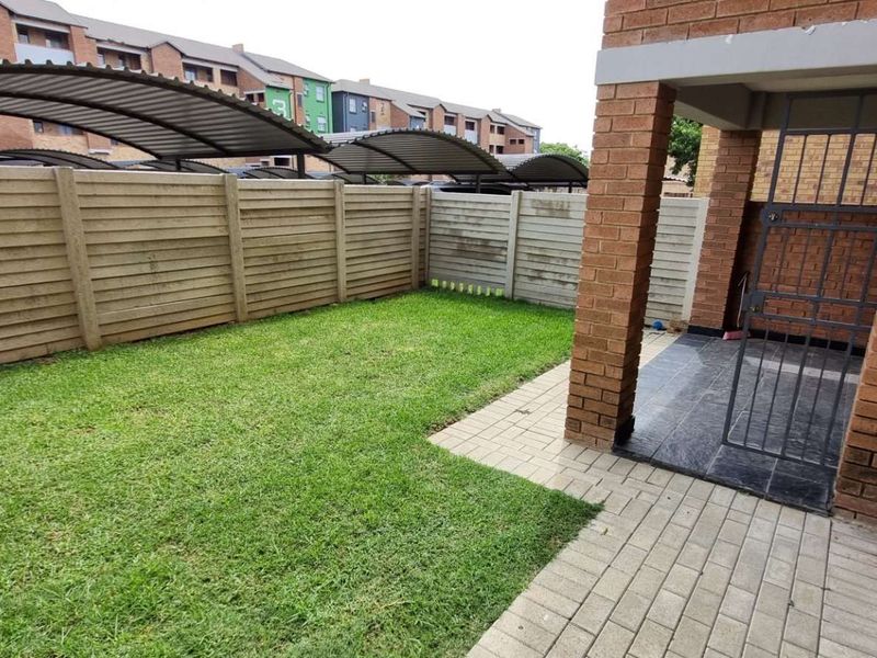 A private rear garden featuring a small paved patio area, a security gate, and a precast concrete boundary wall.