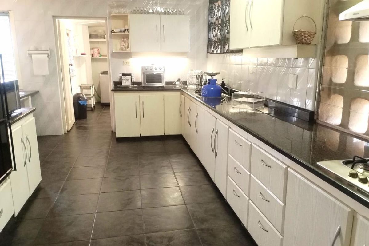 Functional kitchen featuring granite countertops, ample built-in cabinetry, tiled flooring, and a gas hob, with an adjacent scullery area.