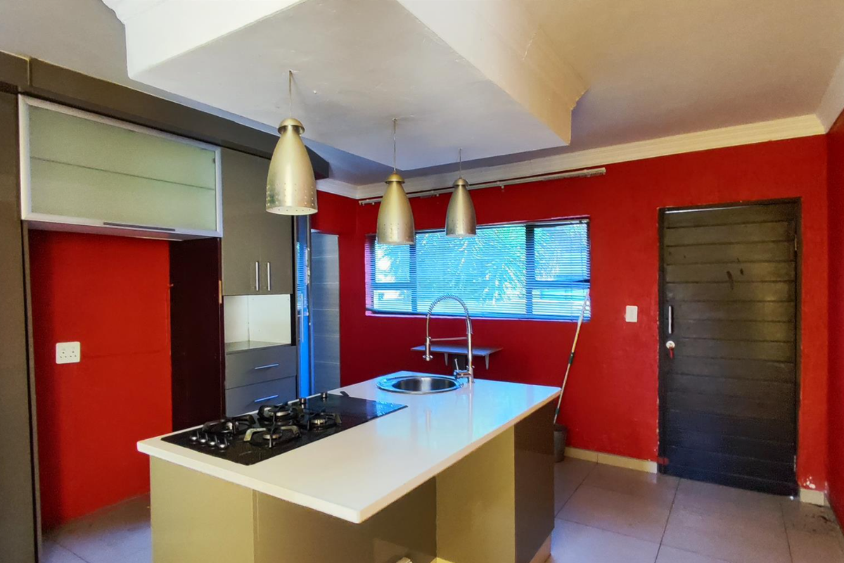 Modern kitchen featuring a central island with a built-in gas hob and sink, complemented by sleek cabinetry and bold red accent walls.