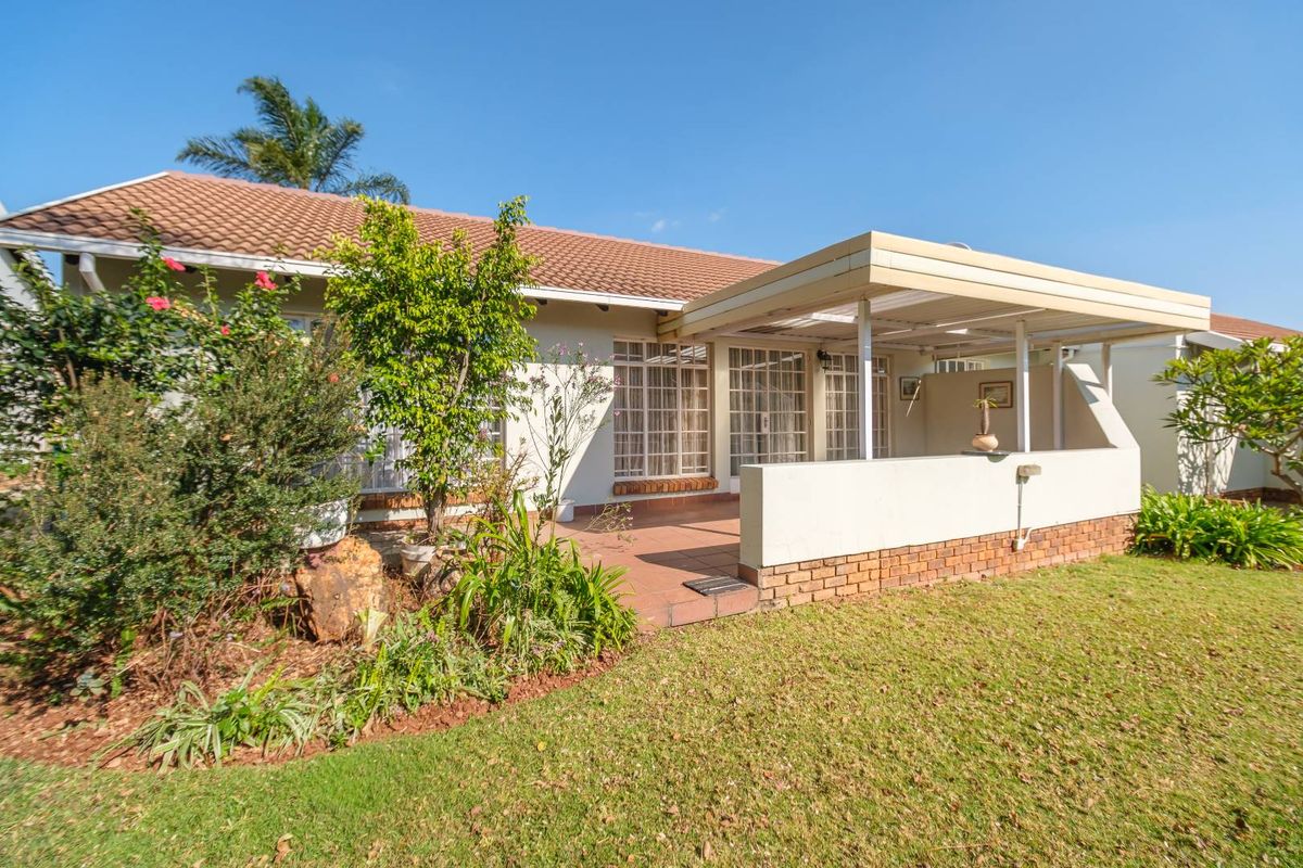Rear view of the townhouse featuring a covered patio area, tiled roof, and a well-maintained garden space.