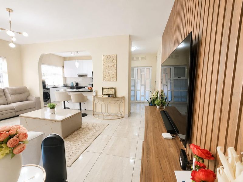 A bright open-plan living area featuring polished tile floors, a modern slatted wood feature wall, and a connected kitchen with contemporary cabinetry.