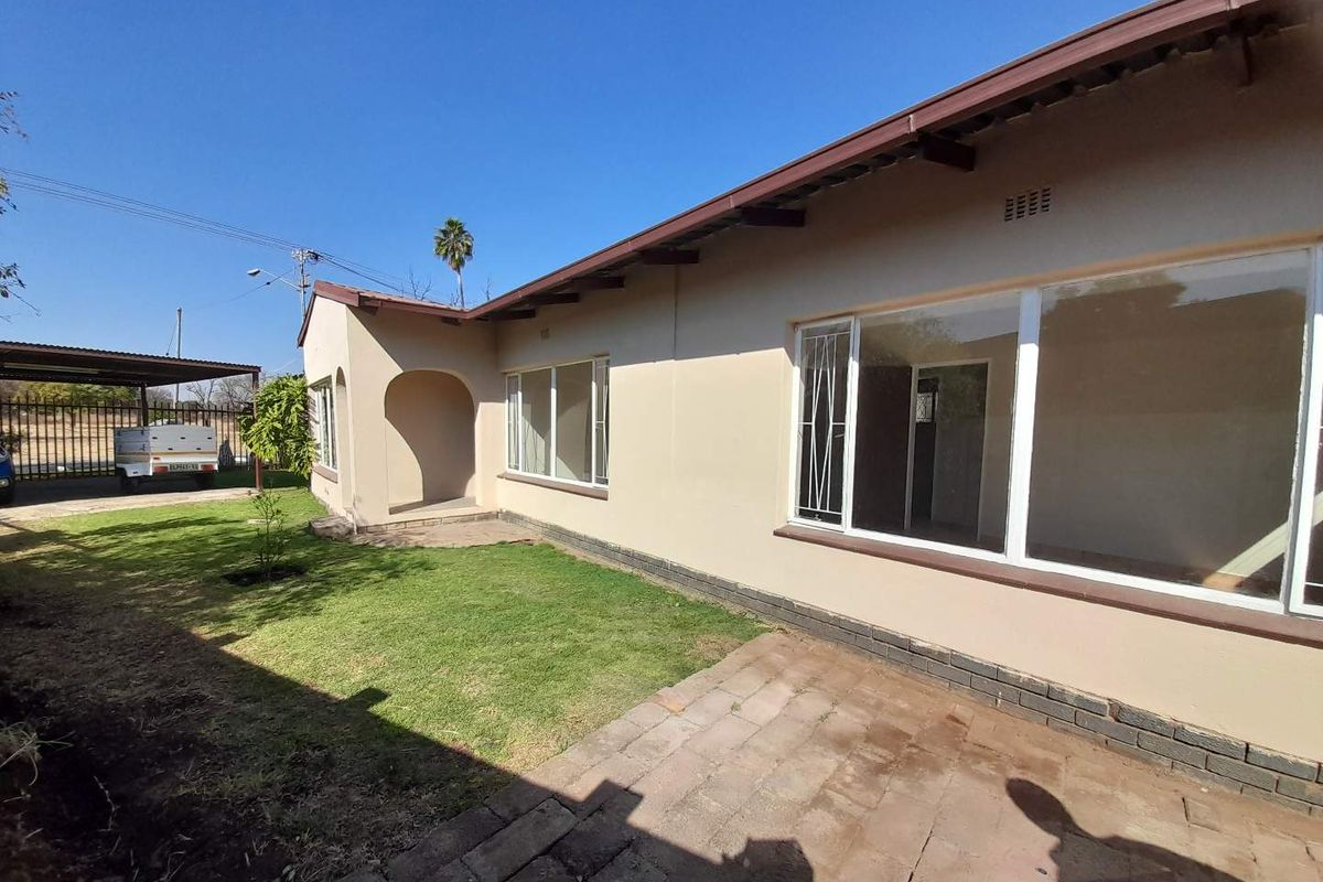 Rear view of the house featuring a paved patio area, established lawn, and aluminum-framed windows with security bars.