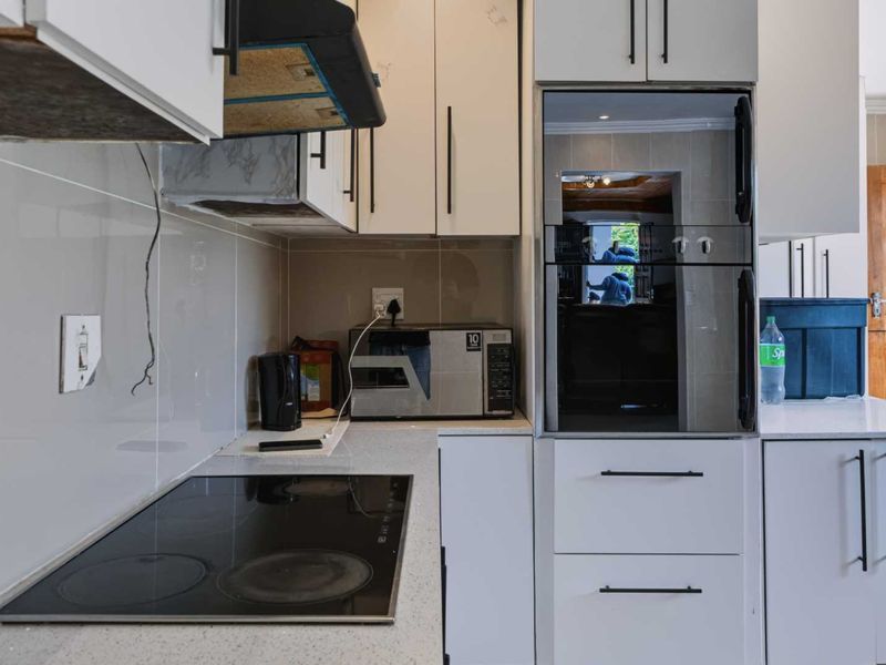 A functional kitchen featuring built-in cabinetry, a modern electric cooktop, integrated oven, and quartz countertops with a tiled splashback.