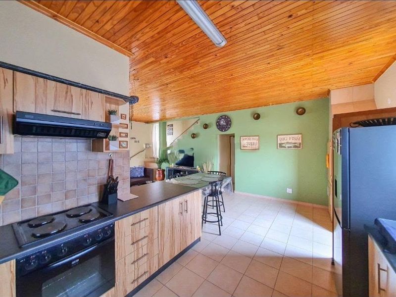 Open-plan kitchen and living area featuring a timber-clad ceiling, tiled flooring, and functional cabinetry with built-in cooking appliances.