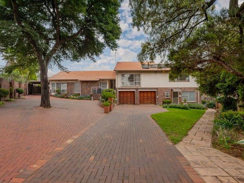 Front view of a multi-level residential property featuring a spacious brick driveway, double garage, and established garden surroundings.