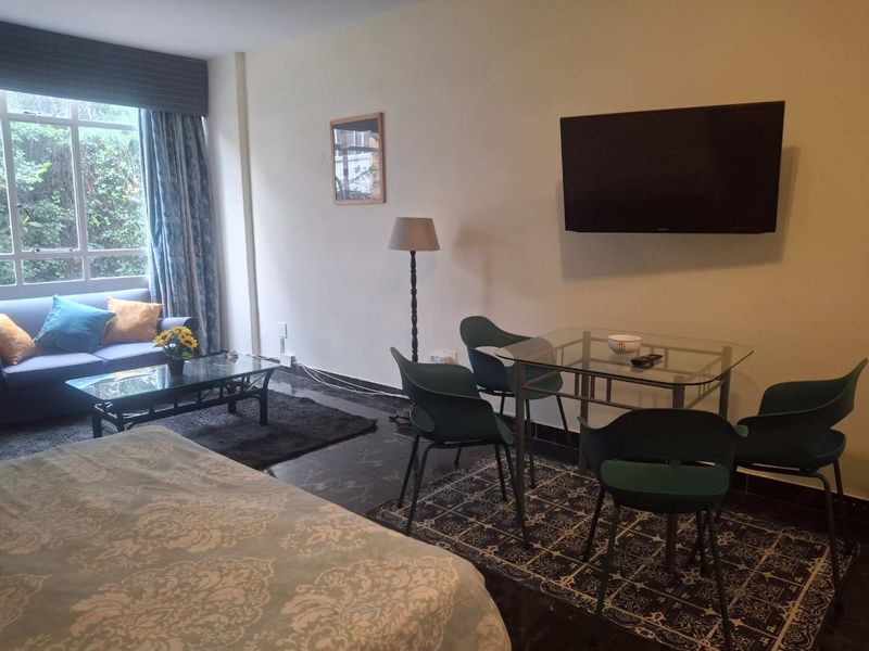 An open-plan living and dining area featuring dark tiled flooring, a large window, and a wall-mounted television.