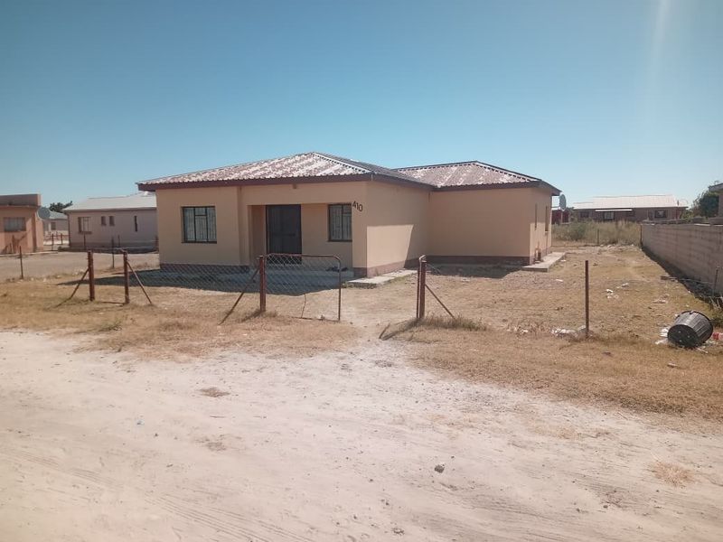 Front view of a single-story detached house featuring a metal roof, security gate, and an unlandscaped yard with wire fencing.