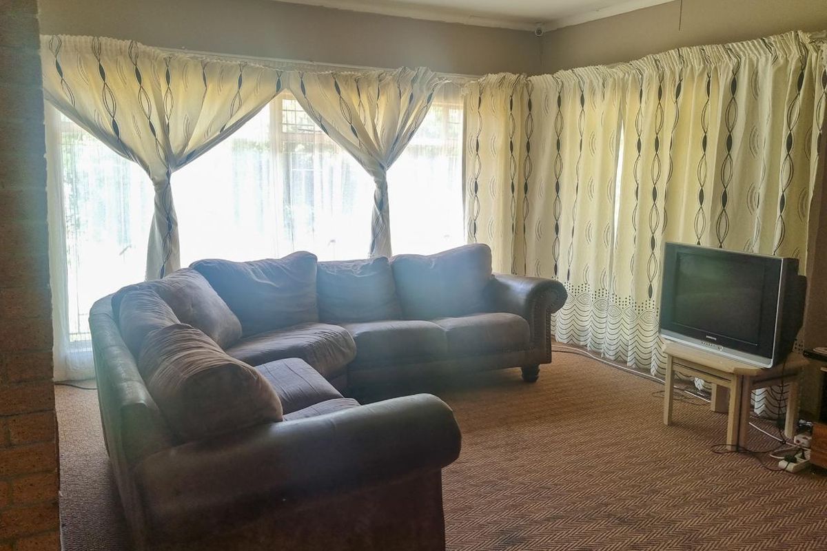 A spacious living room featuring large windows with natural light, carpeted flooring, and a ceiling fan.