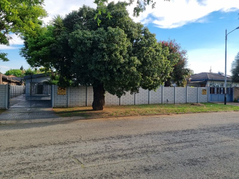 Street view of the property featuring a concrete block boundary wall, mature tree, and gated driveway access.