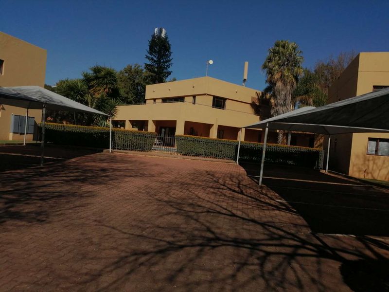 Exterior view of an apartment complex featuring a paved driveway, covered parking carports, and landscaped hedging surrounding the building facade.