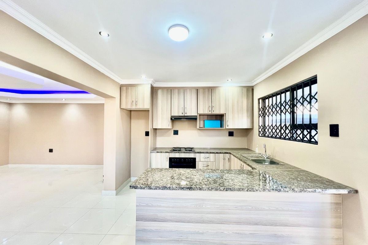 Modern kitchen featuring light wood cabinetry, granite countertops, built-in oven and hob, and an open-plan layout connecting to the living area.