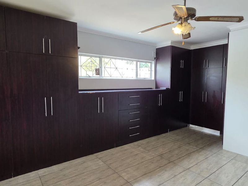 Spacious bedroom featuring extensive dark wood built-in cabinetry, tiled flooring, and a ceiling fan, offering ample storage and a clean, neutral aesthetic.