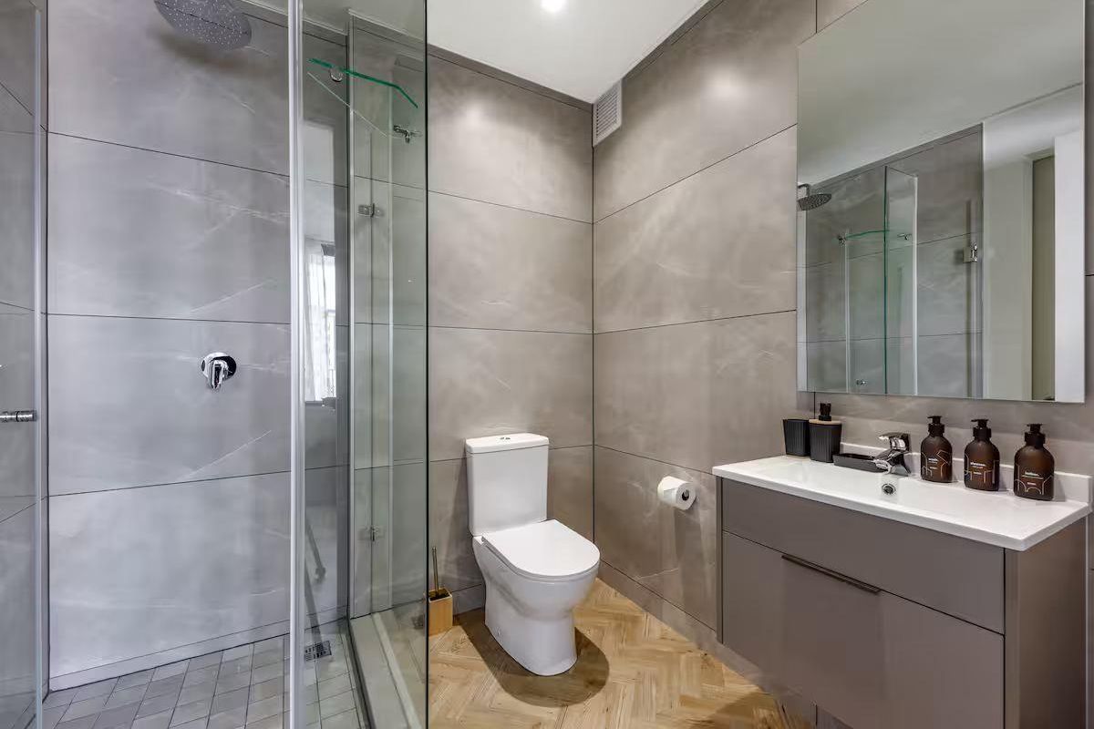 Modern bathroom featuring a walk-in shower with glass screen, vanity cabinet with integrated basin, and stylish herringbone flooring.