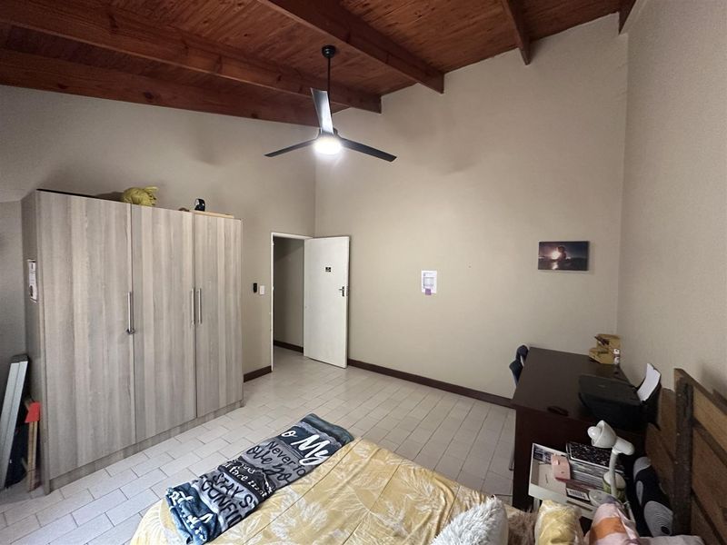A bedroom featuring an exposed timber rafter ceiling, tiled flooring, and a built-in wardrobe.