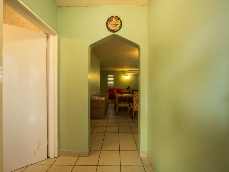 A hallway featuring tiled flooring and an arched doorway leading into the main living area, finished with light green wall paint.