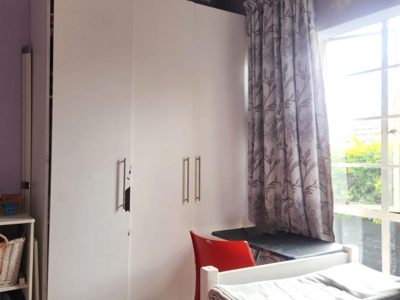 A bedroom featuring a large white built-in wardrobe and a window providing natural light.