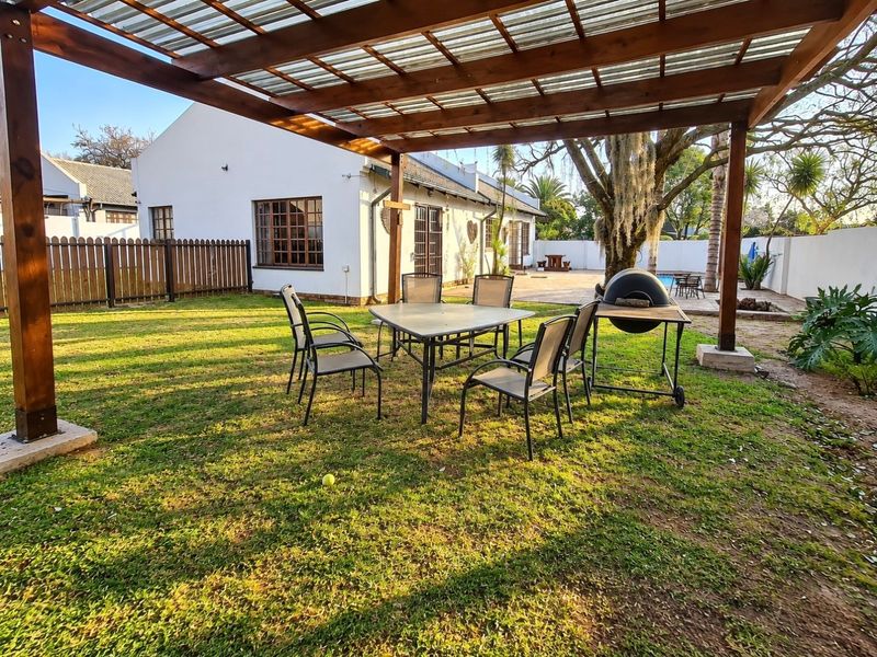 A spacious outdoor patio area featuring a sturdy timber pergola with a translucent roof, overlooking a well-maintained garden and rear building elevation.