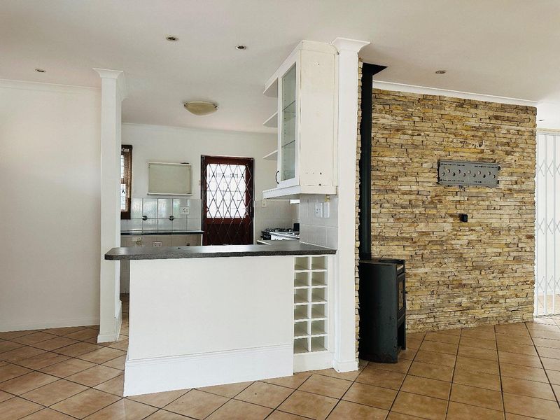 Open plan living area featuring a stone accent wall, a freestanding fireplace, and a kitchen with a breakfast bar and built-in wine storage.