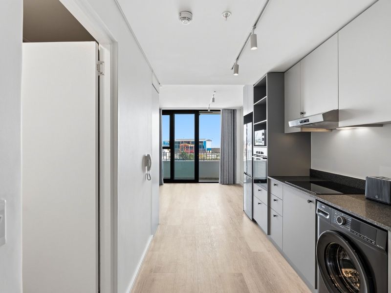 Modern open-plan kitchen and living area featuring sleek cabinetry, integrated appliances, track lighting, and direct access to a private balcony.