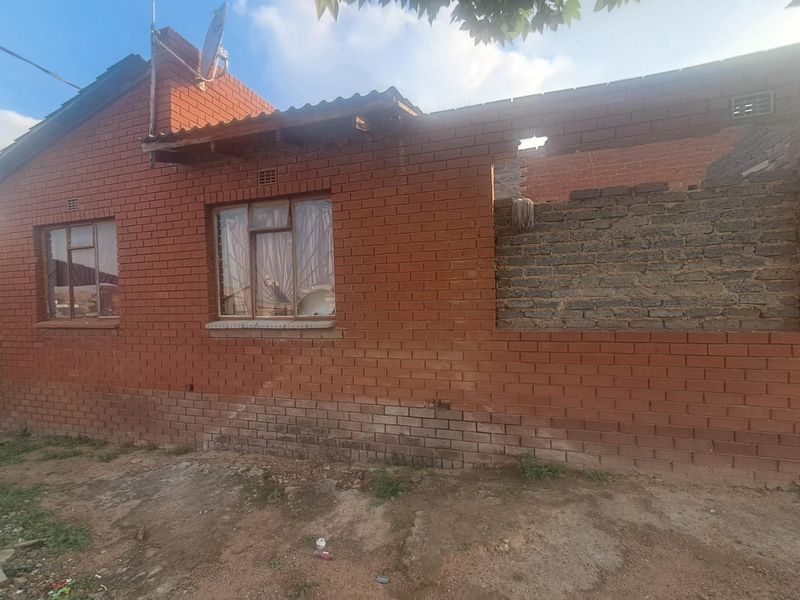 Rear view of a brick house showing incomplete construction, missing roof sections, and exposed masonry walls requiring significant structural repair.