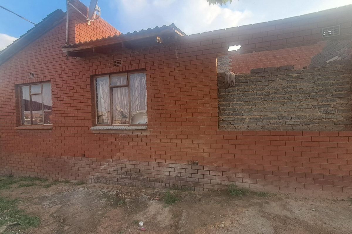 Rear view of a brick house showing incomplete construction, missing roof sections, and exposed masonry walls requiring significant structural repair.