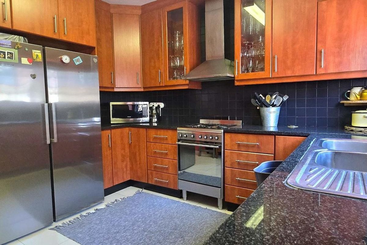 A functional kitchen featuring wooden cabinetry, dark granite countertops, a stainless steel gas stove with extractor fan, and a double-basin sink with a gooseneck faucet.