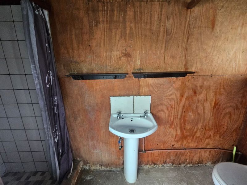 A basic bathroom featuring a pedestal basin, tiled shower area, and toilet, with plywood wall paneling in need of renovation.