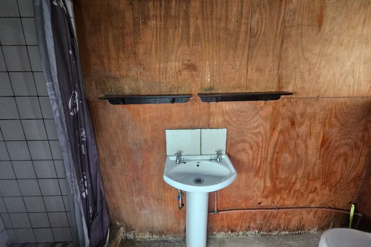 A basic bathroom featuring a pedestal basin, tiled shower area, and toilet, with plywood wall paneling in need of renovation.
