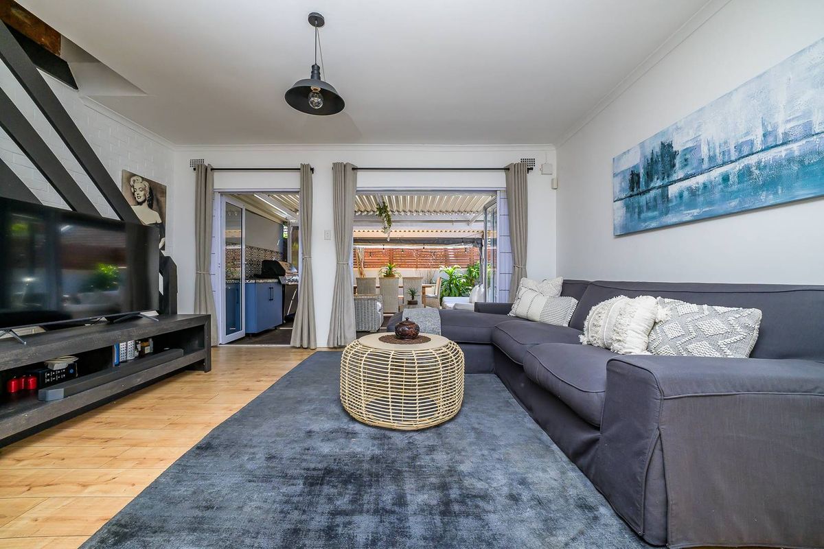 A bright living room featuring light wood flooring, a modern pendant light, and large sliding doors that open onto a covered patio area.