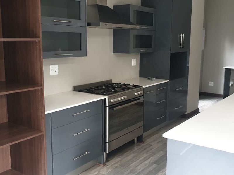 Modern kitchen featuring dark grey cabinetry, stone countertops, a gas stove with extractor fan, and a central island, finished with durable laminate flooring.