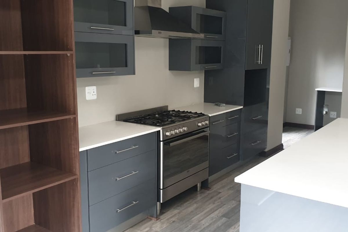 Modern kitchen featuring dark grey cabinetry, stone countertops, a gas stove with extractor fan, and a central island, finished with durable laminate flooring.