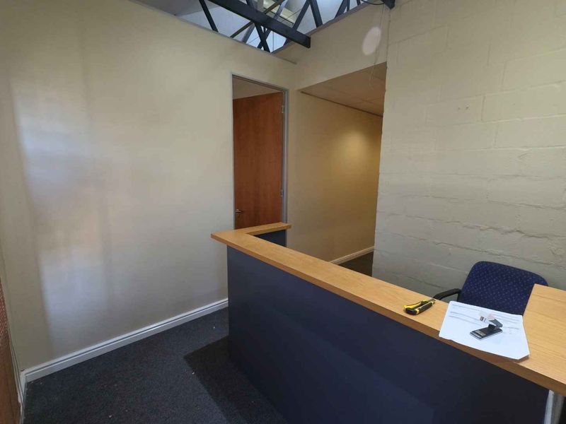 A functional office reception area featuring a built-in desk, carpeted flooring, and exposed roof trusses, providing a practical workspace entry point.