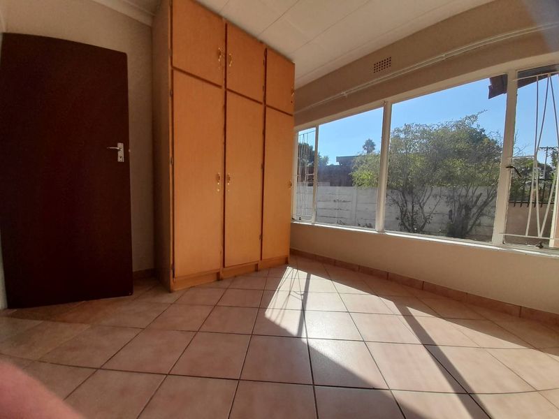 A bright, empty bedroom featuring tiled flooring, large windows for natural light, and built-in wooden cupboards.