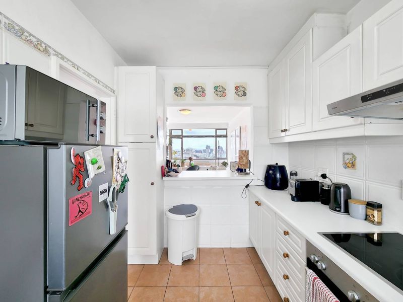 A functional kitchen featuring white cabinetry, tiled backsplash, and a convenient pass-through window overlooking the living area and city views.