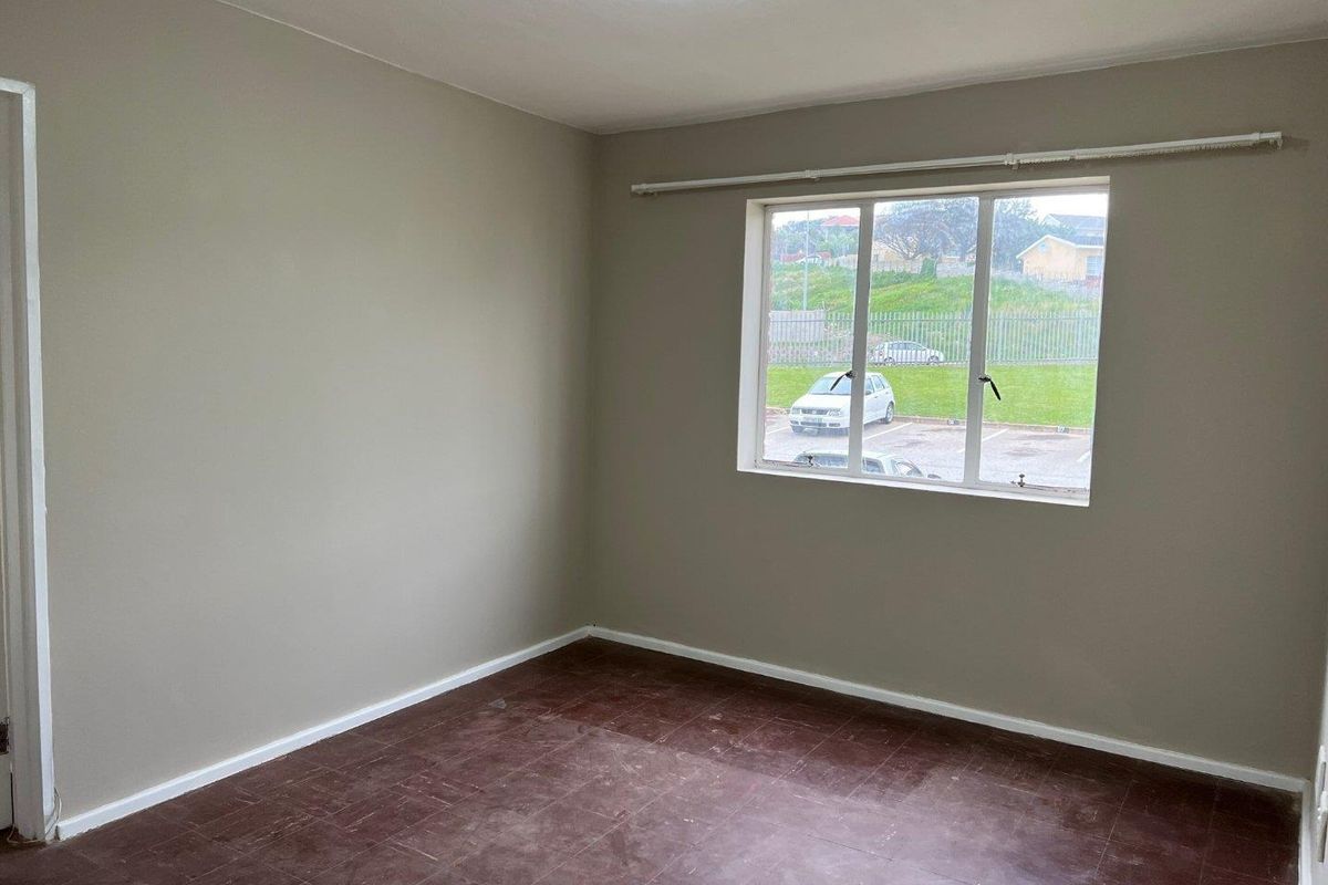 An empty bedroom featuring neutral wall paint, tiled flooring, and a window with a curtain rail, offering a blank canvas for personalization.